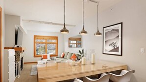 A modern kitchen with a wooden table and white chairs, a fireplace, and a large window. - Incredible Snowmass Condo by Gondola! Walk to Dining & Shops. A/C, Hot Tubs, Balcony, W/D, Parking! (Snowmass Village)