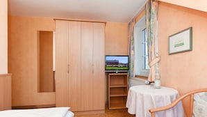 Un dormitorio con cama, armario, televisor, mesa con silla y ventana con cortinas.