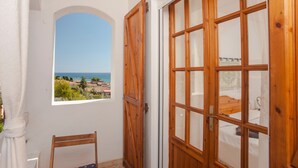 Una habitación con puerta de madera, ventana con vista al mar y una silla.