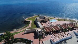 Vista aérea de un hotel costero con piscina, asientos al aire libre y vista al océano.