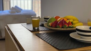 Una tavola imbandita per la colazione, con una ciotola di frutta, un bicchiere di succo d'arancia e un letto sullo sfondo.