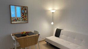 Un soggiorno moderno con un divano bianco, un tavolo da pranzo in legno con sedie, una ciotola di frutta e un lampadario a parete.