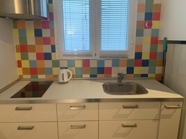 Una cocina con un respuesto de azulejos de colores, una ventana con persianas, un hervidor y un lavamanos.