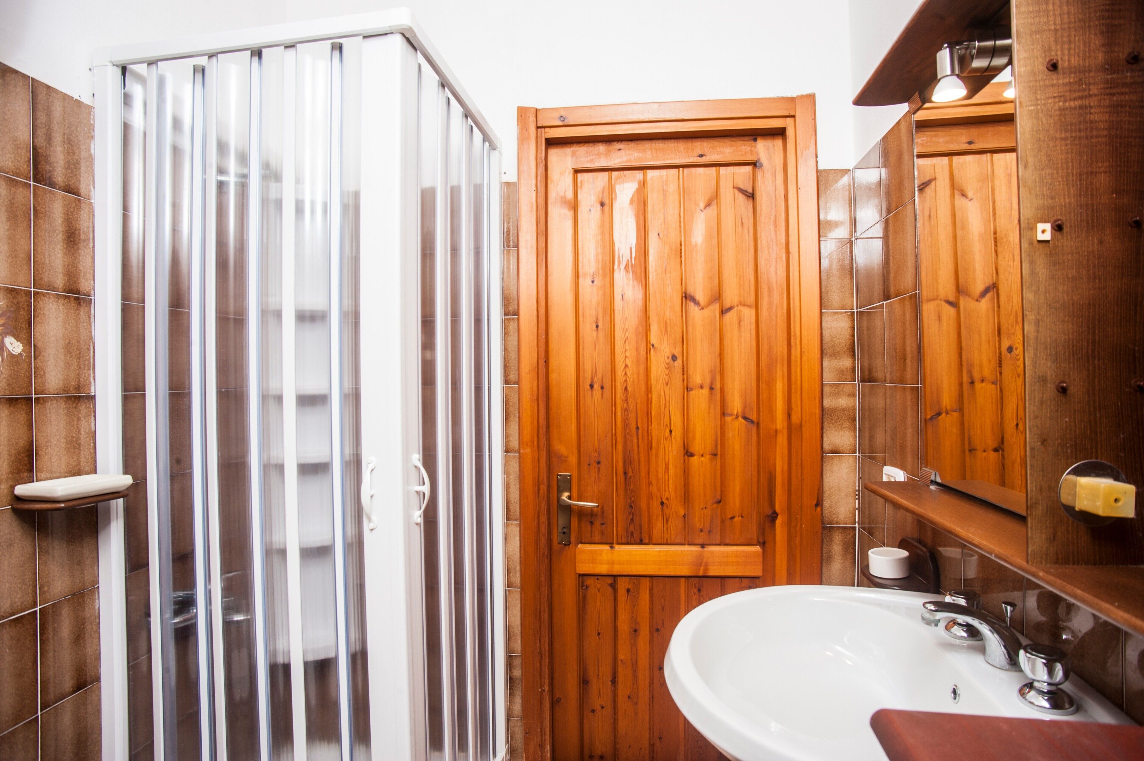 A bathroom with a wooden door, a shower enclosure, a sink, and a mirror.