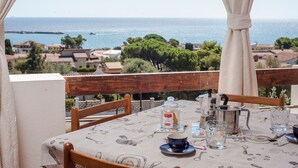 A table set with a coffee pot, cups, and glasses, overlooking a coastal view with houses and trees.