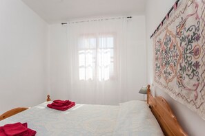 Ein Schlafzimmer mit einem Bett, einem Fenster mit durchsichtigen Vorhängen, einer Wandteppich und einer Nachttischlampe.
