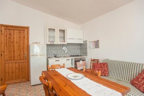 Eine kompakte Küche mit Kühlschrank, Herd und Schränken, ein Holztisch mit Stühlen und ein kariertes Sofa.