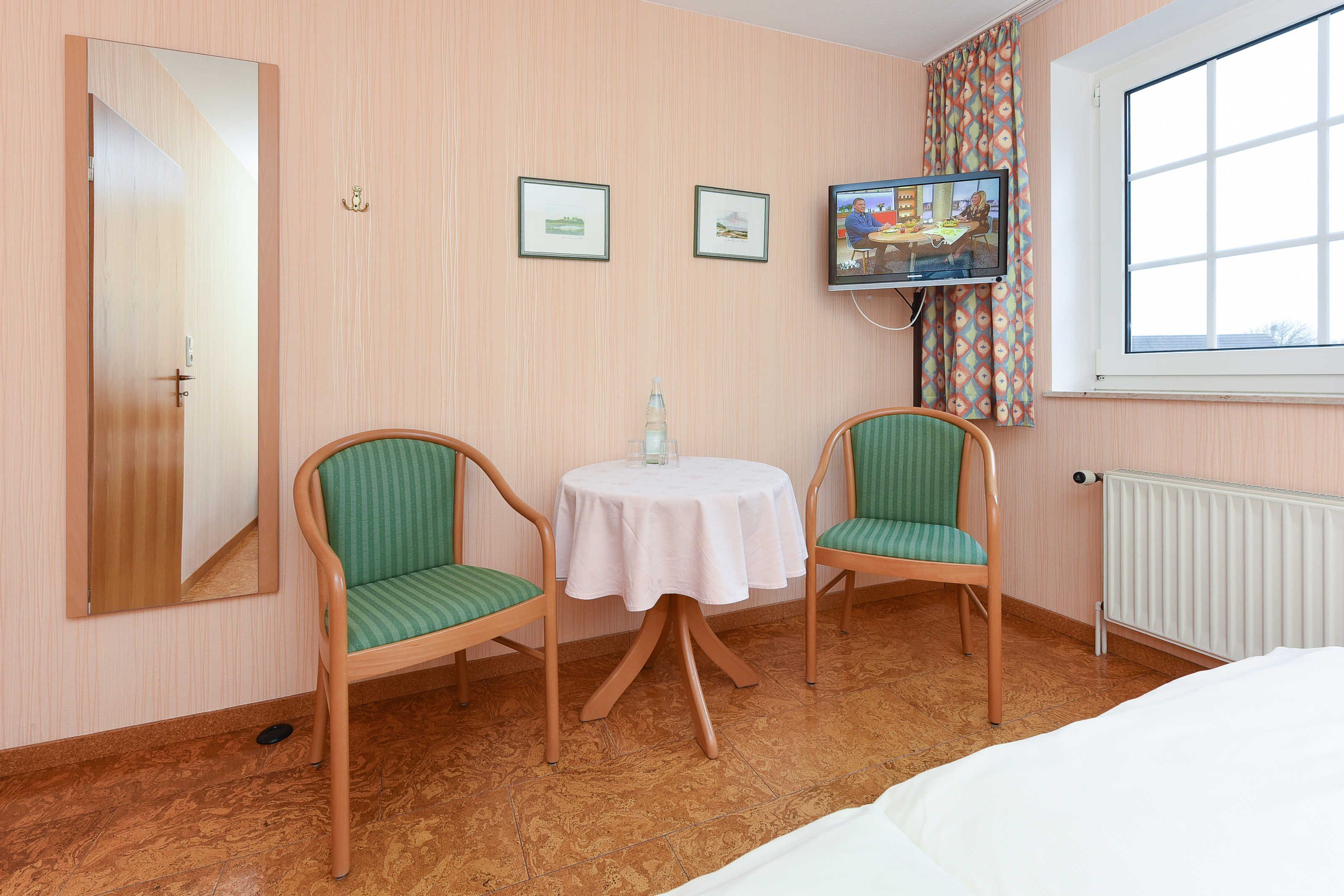 Una camera d'albergo con due poltrone a righe verdi attorno a un tavolino, un letto, una TV a parete e una finestra con vista.