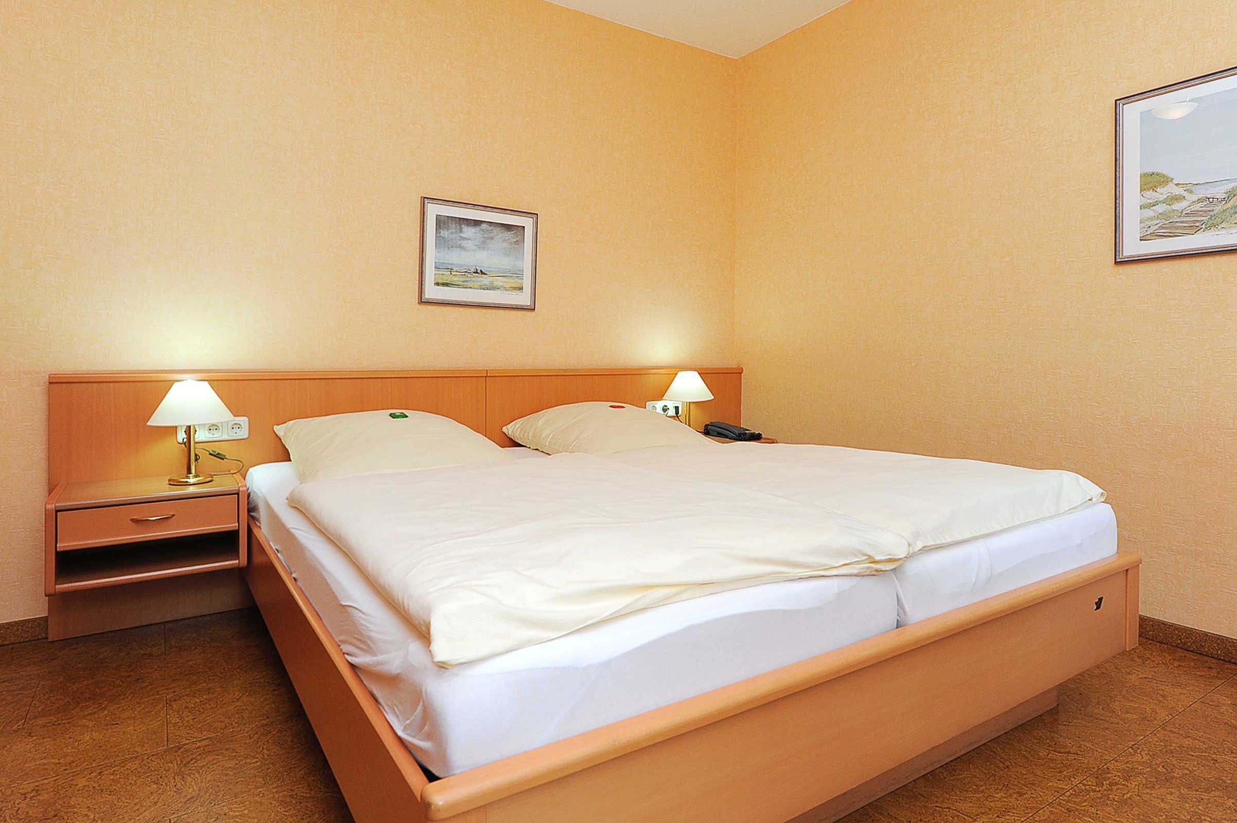 Camera d'albergo con un letto singolo, due comodini con lampade, un quadro appeso al muro e una parete spoglia.