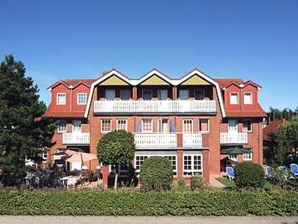Un hôtel à plusieurs étages, doté d’une façade symétrique, de balcons et d’un jardin bien entretenu.