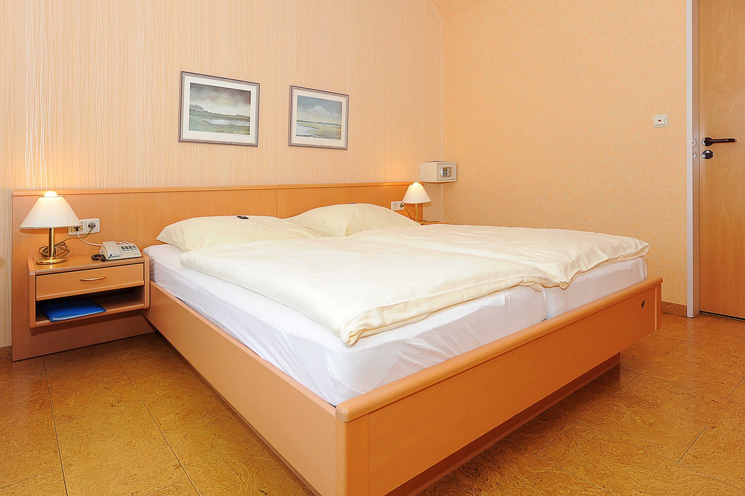 A single bed with a wooden frame, two bedside tables with lamps, and two framed pictures on the wall.