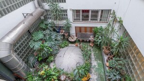 Un patio con plantas en macetas, un banco de madera y una estructura metálica.