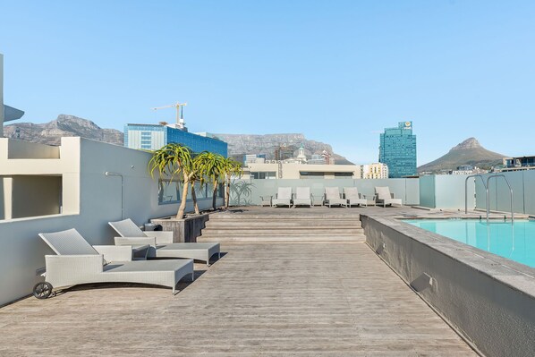 A rooftop pool area with lounge chairs and a view of the cityscape and mountains.