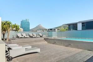 A rooftop pool area with lounge chairs, a pool, and a view of a mountain and a building in the background.