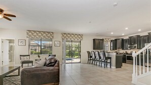 A spacious living area with a brown leather sofa, a dining table with chairs, and a kitchen with dark cabinets and a stainless steel range hood. - Imagine You and Your Family Renting This 5 Star Villa on Champions Gate Resort, Orlando Villa 3611 (Davenport)