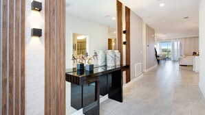 A modern interior with a glass-top console table, wooden paneling, and a view of a dining area.