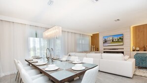 A modern dining area with a glass table, white chairs, and a chandelier.