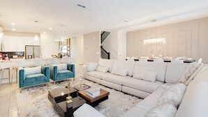 A modern living room with a large sectional sofa, a coffee table, and a kitchen area in the background.
