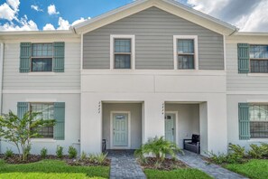 A two-story residential building with a central entrance, a covered porch, and a small garden area. - The Secret to Enjoying Your Luxury Townhome on Windsor at Westside Resort, Orlando Townhome 3637 (Kissimmee)