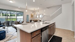 Une cuisine moderne dotée d’un grand îlot central, d’appareils électroménagers en acier inoxydable et de luminaires suspendus.