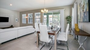A modern dining area with a central table, white chairs, and a chandelier.