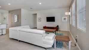 A modern living room with a white sectional sofa, a wooden coffee table, and a flat-screen TV mounted on the wall.