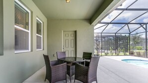 A covered patio with a table and chairs, a pool, and a view of the outdoors.