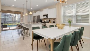 A modern kitchen with white cabinets, a large island, and bar stools. - Your Family Will Love the 1st Class Amenities at Your Private Villa on Solterra Resort, Orlando Villa 3683 (Davenport)