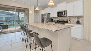 A modern kitchen with a large island, bar stools, stainless steel appliances, and a view of a swimming pool. - Your Family Will Love the 1st Class Amenities at Your Private Villa on Solterra Resort, Orlando Villa 3683 (Davenport)