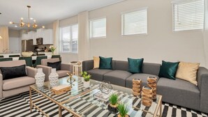 A modern living room with a sofa, coffee table, and kitchen in the background. - Your Family Will Love the 1st Class Amenities at Your Private Villa on Solterra Resort, Orlando Villa 3683 (Davenport)
