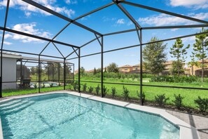 Uma piscina com cobertura de vidro, rodeada por gramado e árvores.