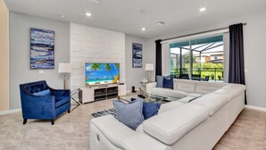 A modern living room with a white sectional sofa, a blue armchair, and a flat-screen TV on a white entertainment unit. - Luxury 5 Star Villa on Solterra Resort, Orlando Villa 3692 (Davenport)