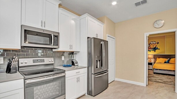A modern kitchen with white cabinets, stainless steel appliances, and a visible clock on the wall. - Rent the Perfect Luxury Villa on Champions Gate Resort, Orlando Villa 3707 (Davenport)