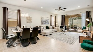 A modern living room with a dining area, a sofa set, a chandelier, and a ceiling fan.