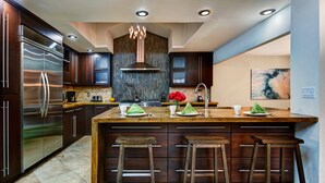 Une cuisine moderne avec des meubles en bois foncé, des appareils électroménagers en acier inoxydable, un îlot central doté de tabourets et un luminaire décoratif.