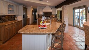 A spacious kitchen with granite countertops, a central island with fruit, and a view to the outdoors. - Royal Palms (Phoenix)