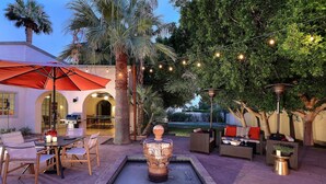 An outdoor patio area with a dining table, chairs, a red umbrella, a decorative fountain, and string lights. - Royal Palms (Phoenix)
