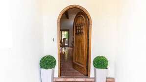 A wooden door with a black handle, flanked by two white planters with green shrubs, and a doormat with the text "Home sweet home". - Royal Palms (Phoenix)