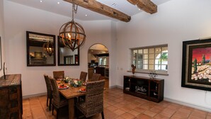 A dining area with a wooden table and wicker chairs, a hanging light fixture, and a view of the kitchen through an archway. - Royal Palms (Phoenix)