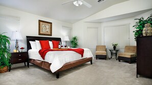Une chambre à coucher avec un grand lit, des tables de chevet, une chaise, une petite table et une plante en pot.