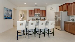 A modern kitchen with white bar stools, wooden cabinets, stainless steel appliances, and recessed ceiling lights. - Picture Renting Your Own Luxury Villa on the Exclusive Solterra Resort, Close to Disney, Orlando Villa 3690 (Davenport)