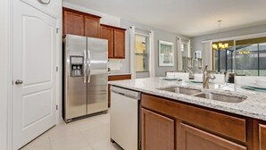A modern kitchen with a stainless steel refrigerator, wooden cabinets, a granite countertop, and a double sink. - Picture Renting Your Own Luxury Villa on the Exclusive Solterra Resort, Close to Disney, Orlando Villa 3690 (Davenport)