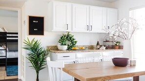 A modern kitchen with white cabinetry, a wooden dining table, and a potted plant. - Perfect 4 Bdrm Home With Pool and Game Room! (Phoenix)