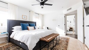 A modern bedroom with a large bed, a ceiling fan, and a view into the bathroom. - Perfect 4 Bdrm Home With Pool and Game Room! (Phoenix)