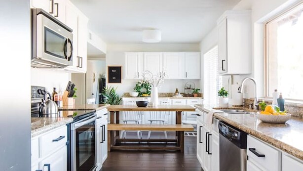A modern kitchen with white cabinets, a built-in oven, a microwave, and a dishwasher. There is a wooden bench and a potted plant on the counter. - Perfect 4 Bdrm Home With Pool and Game Room! (Phoenix)