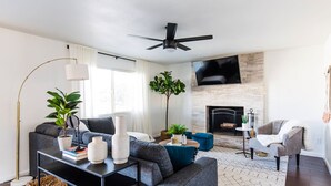 A modern living room with a fireplace, a flat-screen TV, and a ceiling fan. - Perfect 4 Bdrm Home With Pool and Game Room! (Phoenix)