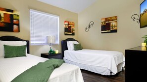 A hotel room with two beds, a window with blinds, a nightstand with a lamp, and artwork on the walls. - Backyard Playground! Golf Sport Court & Hot Tub! (Glendale)