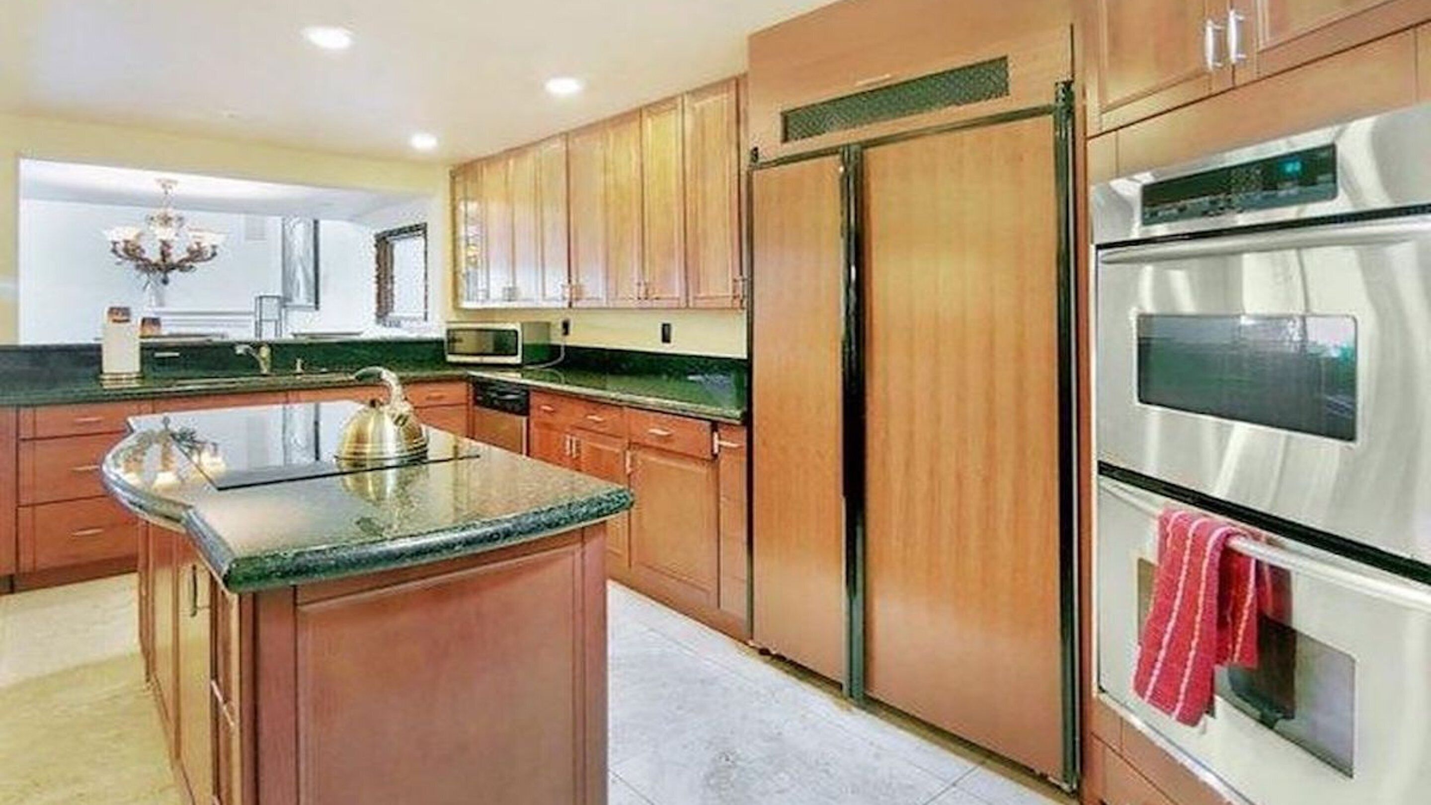A kitchen with wooden cabinets, a stainless steel refrigerator, an oven, and a granite countertop.