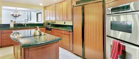 A kitchen with wooden cabinets, a stainless steel refrigerator, an oven, and a granite countertop.