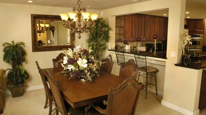 A dining area with a wooden table, chairs, a chandelier, a mirror, and a potted plant. - The Palm (Scottsdale)
